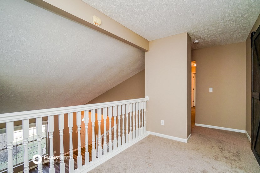 a loft with a white railing and a hallway with a door