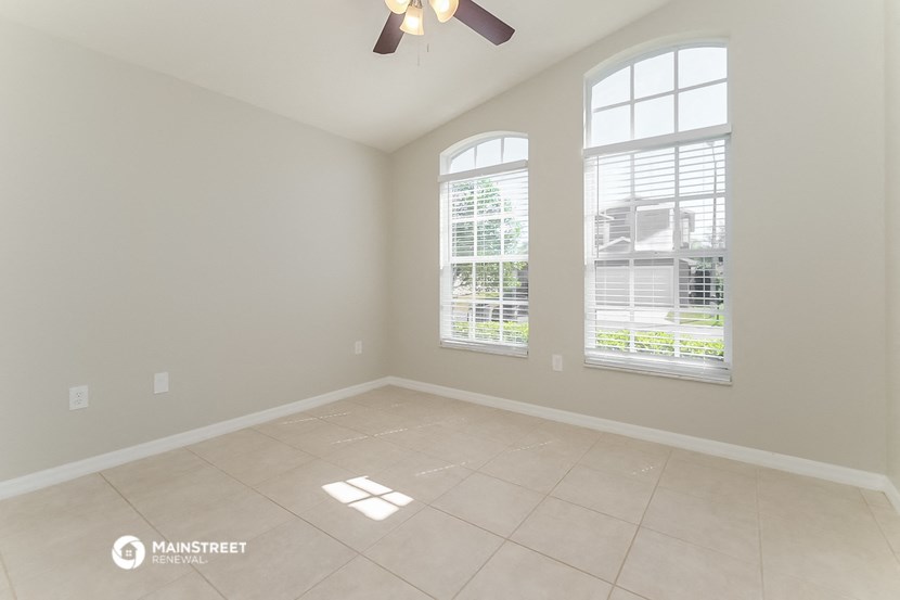 an empty living room with three windows and a ceiling fan