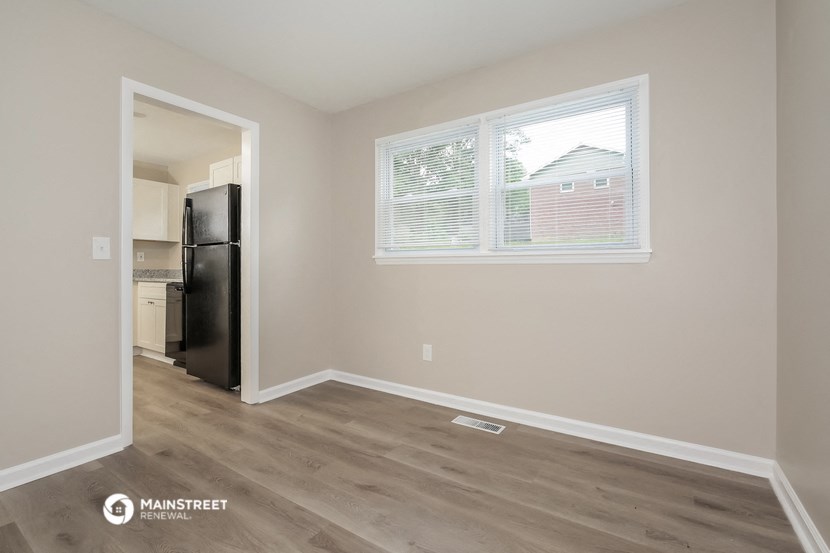 the living room of an apartment with a large window and wood flooring