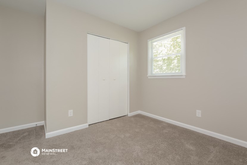 a bedroom with a closet and a window and a carpeted floor