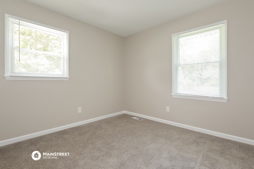 an empty room with two windows and a carpet