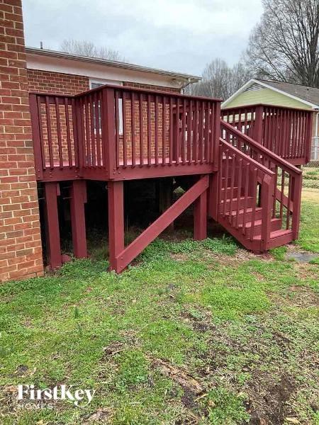 A red wooden deck with a staircase is in front of a brick building.