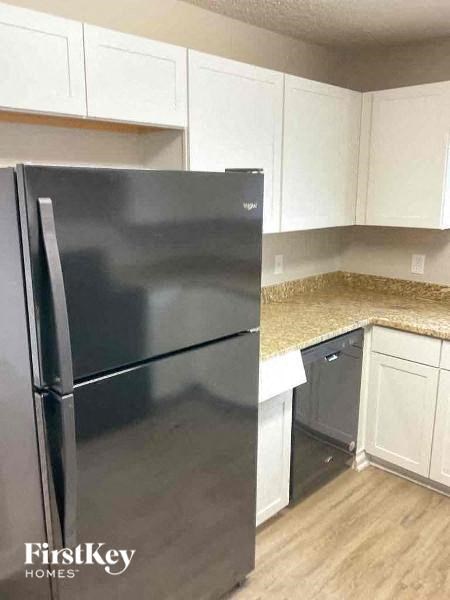 A black fridge in a kitchen with white cabinets.