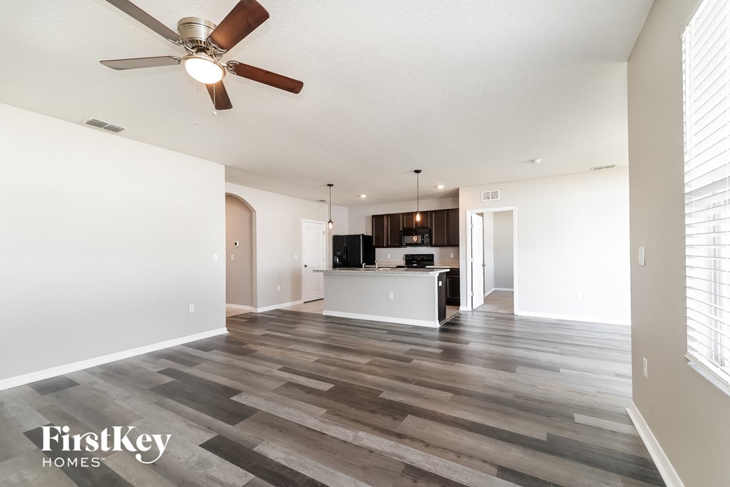 A spacious living room with a ceiling fan and wooden flooring.