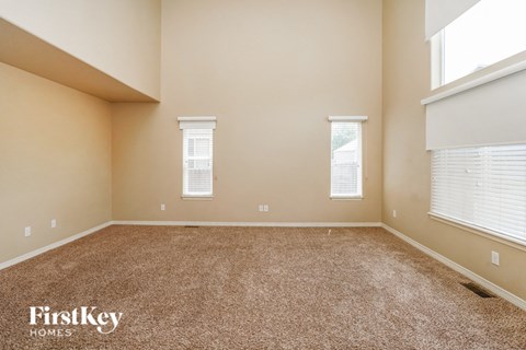 a spacious living room with carpet and two windows