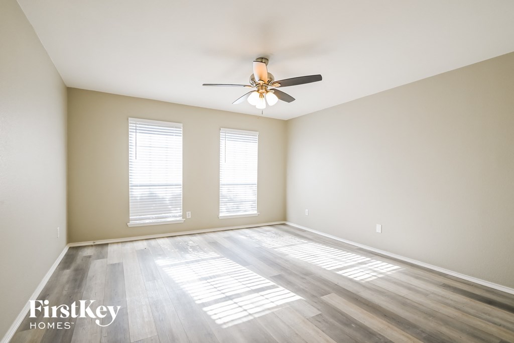 an empty room with a ceiling fan and two windows