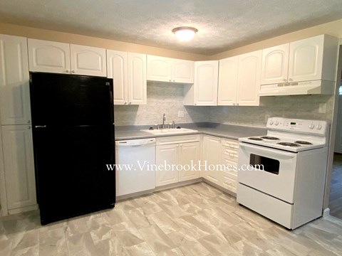 A black refrigerator stands in a kitchen with white cabinets and a white stove.