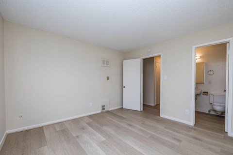 A room with a white door and a bathroom visible through the door.