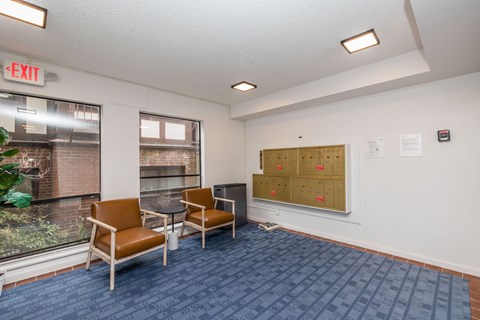 A room with a blue carpet and a white wall with a bulletin board and two chairs.