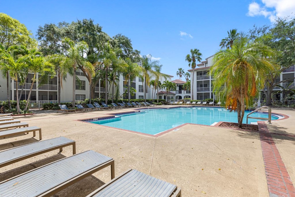 a swimming pool with benches and palm trees in front of an apartment building