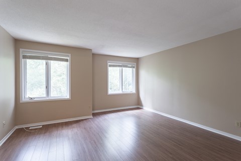 an empty living room with wood floors and two windows