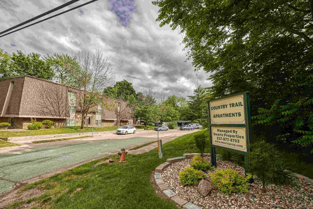A sign for Country Trail Apartments is in front of a grassy area.
