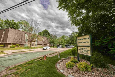 A sign for Country Trail Apartments is in front of a grassy area.