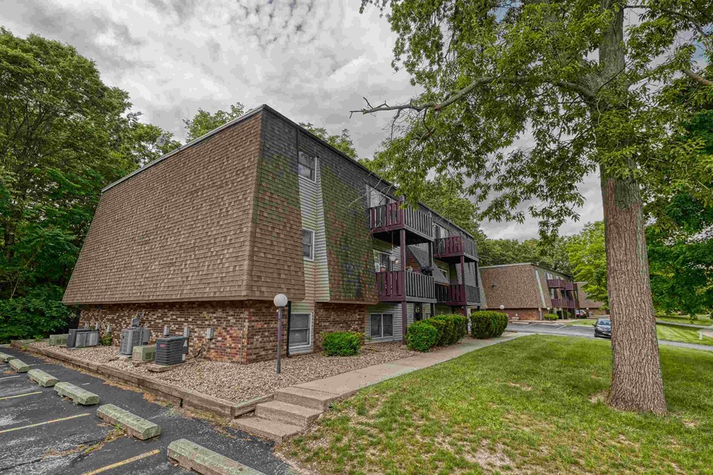 A building with a green and brown facade is surrounded by trees and a parking lot.