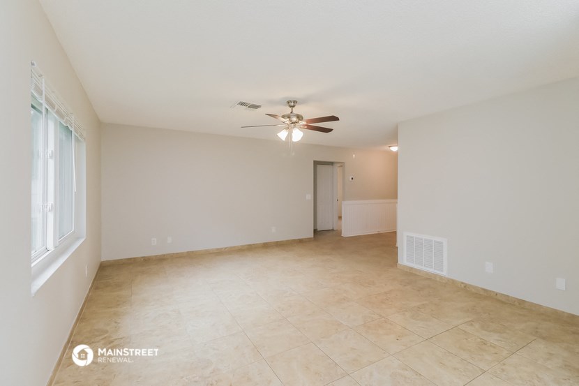 an empty living room with a ceiling fan and tiled floors