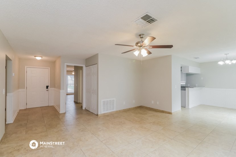 an empty living room with a ceiling fan and a kitchen