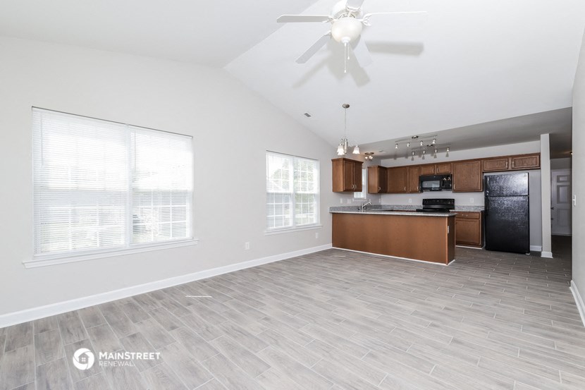 an empty living room with a kitchen and a ceiling fan