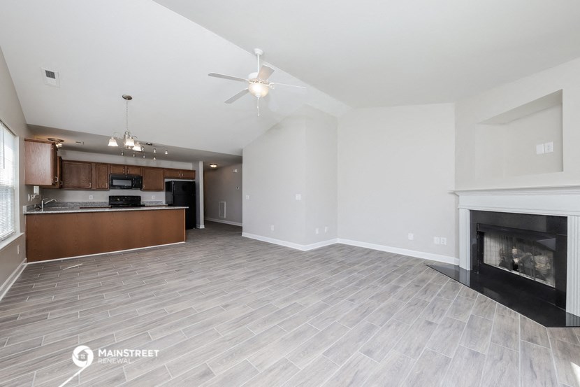 an empty living room with a fireplace and a kitchen