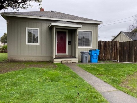 A small house with a red door and a blue trash can.