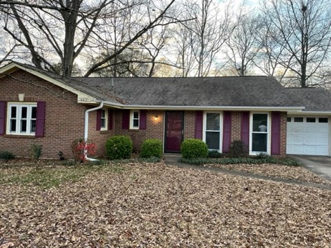 a brick house with purple shutters and a gravel driveway