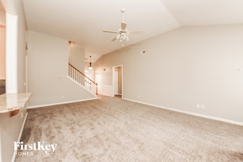 A spacious, empty room with a staircase and a ceiling fan.