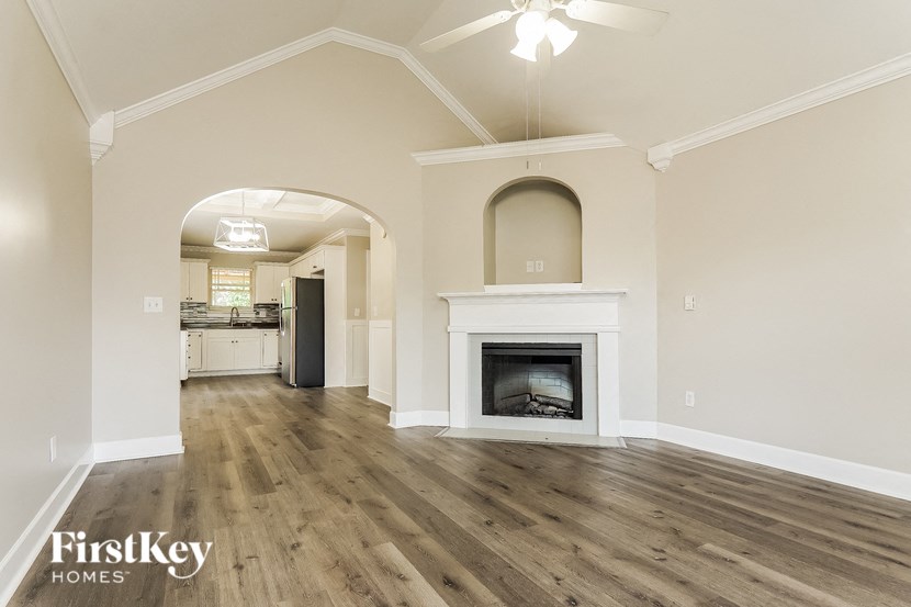 A spacious living room with a fireplace and a kitchen in the background.
