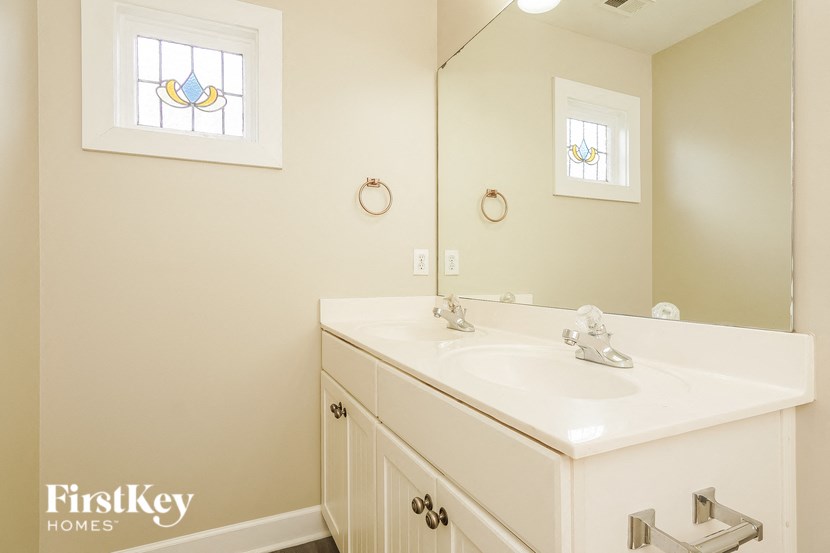 A white bathroom vanity with a mirror and a stained glass window.