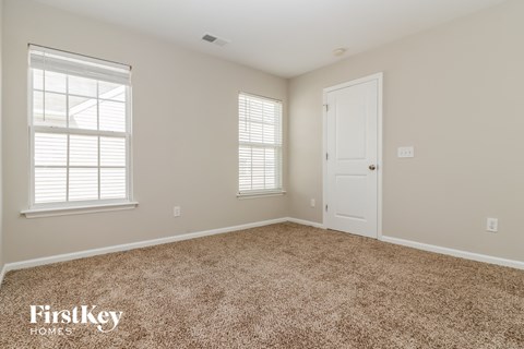 a bedroom with carpet and a door and two windows