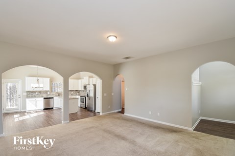 A spacious living room with a kitchen in the background and a carpet on the floor.