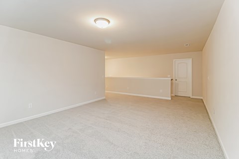 A spacious, empty room with a carpeted floor and a single light fixture on the ceiling.