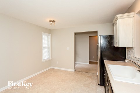 A kitchen area with a sink, refrigerator, and a window with blinds.