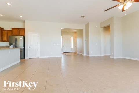 A spacious living room with a kitchen in the background and a ceiling fan.