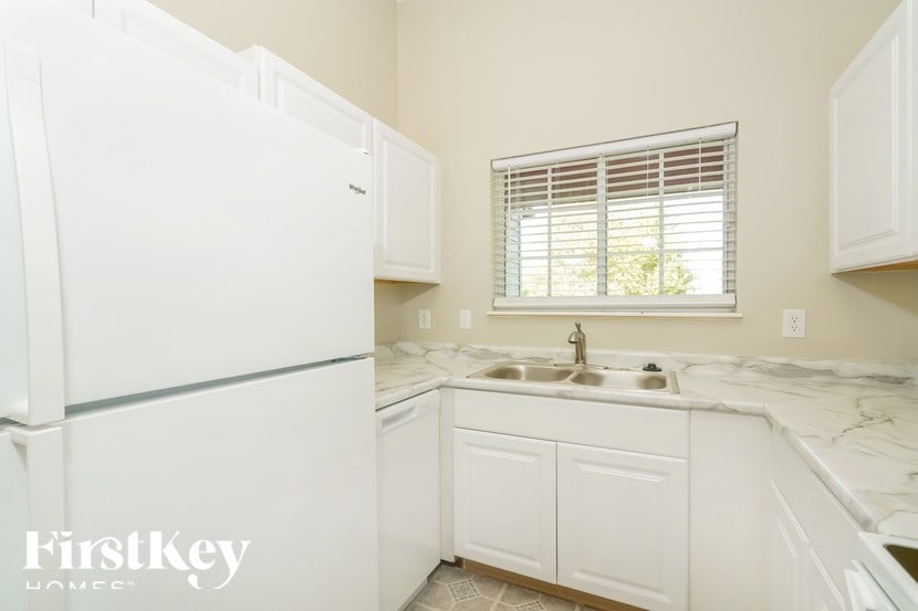 A white kitchen with a refrigerator, sink, and cabinets.