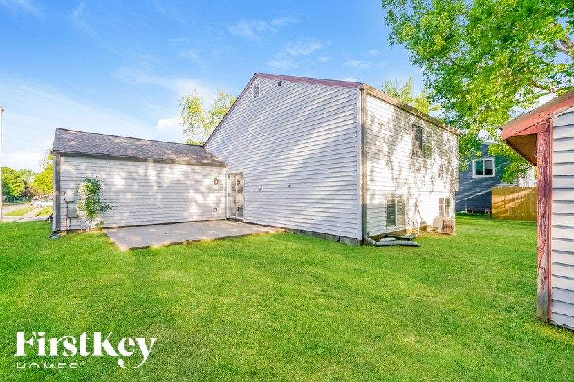 A FirstKey homes sign is on a grassy yard with a metal building.
