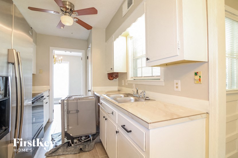 A kitchen with a fan on the ceiling and a refrigerator on the left.