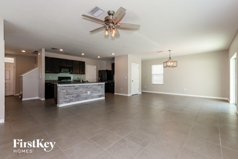A spacious kitchen and living room with a ceiling fan and lighting fixtures.