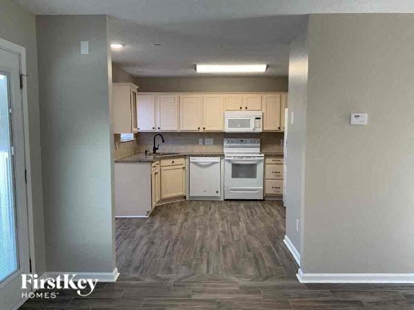 an empty kitchen with white appliances and wooden floors