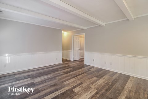 A room with wooden flooring and white walls, with a doorway leading to another room.
