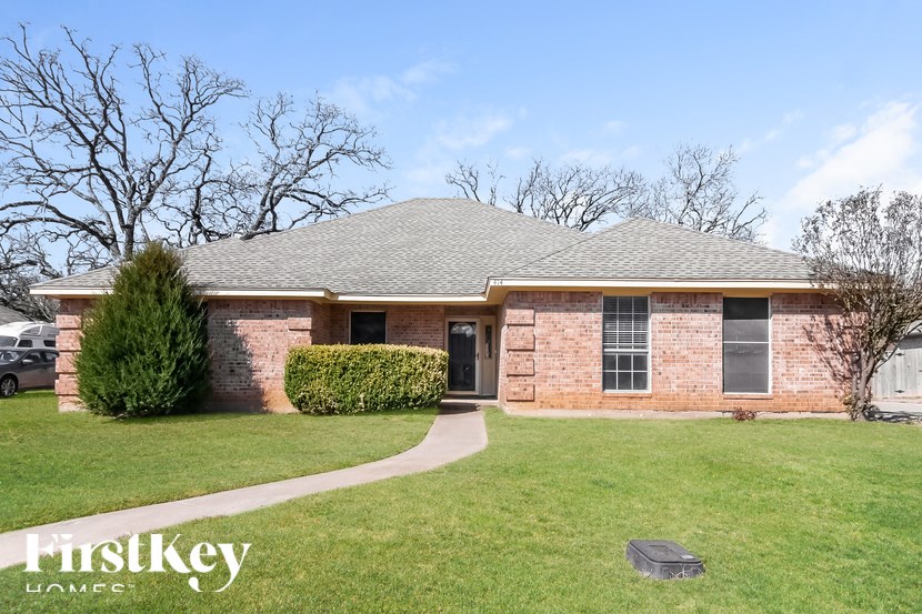 A brick house with a grey roof and a small tree in front.