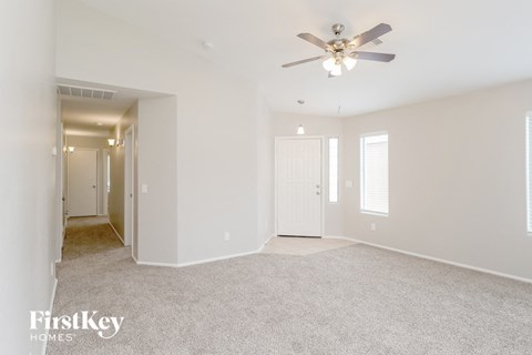 a spacious living room with white carpet and a ceiling fan