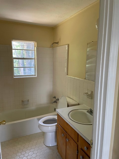 A white toilet sits in a bathroom with a white sink and a bathtub.