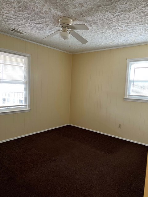 A room with a ceiling fan and two windows.
