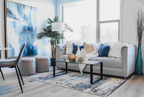A living room with a grey couch, a blue rug, and a large painting on the wall.
