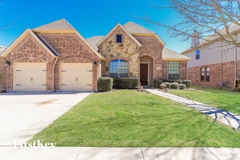 front view of a brick house with white garage doors and a lawn