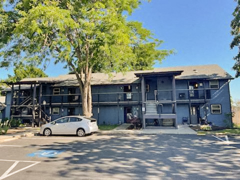 A white car is parked in a parking lot in front of a grey building.