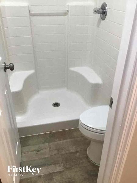 A white tiled bathroom with a toilet and a walk-in shower.