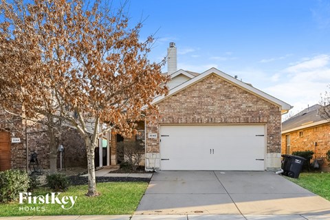 A brick house with a garage and a tree with brown leaves.