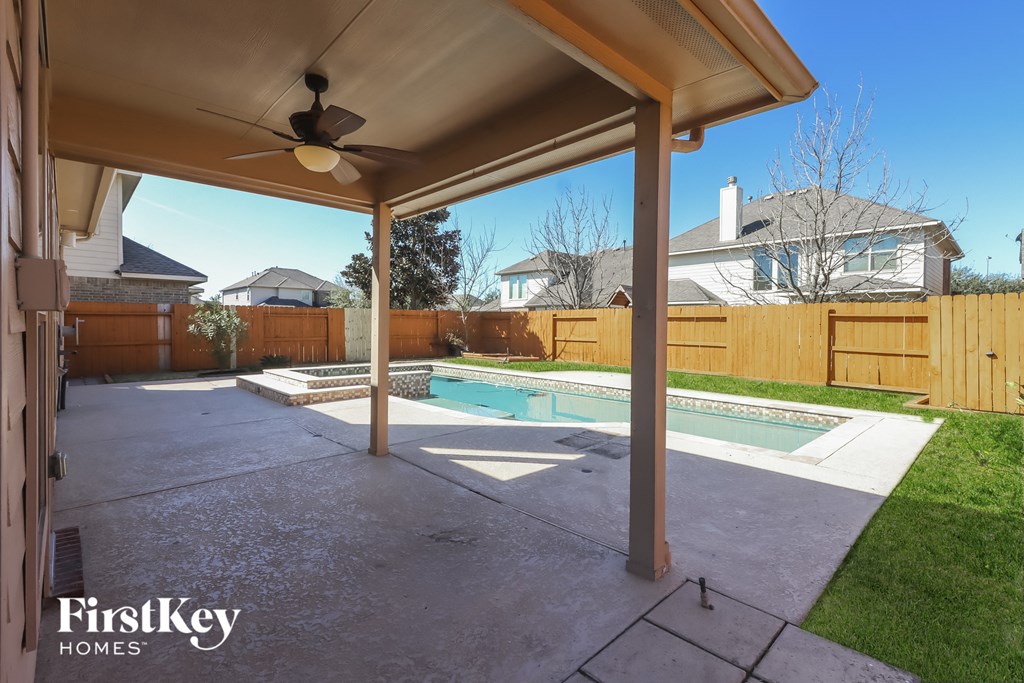 a backyard with a pool and a covered patio with a ceiling fan
