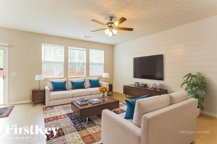 A living room with a white couch, a coffee table, and a flat screen TV mounted on the wall.