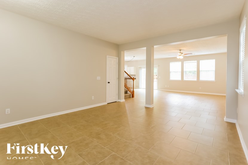 A spacious room with a tiled floor and a staircase in the background.